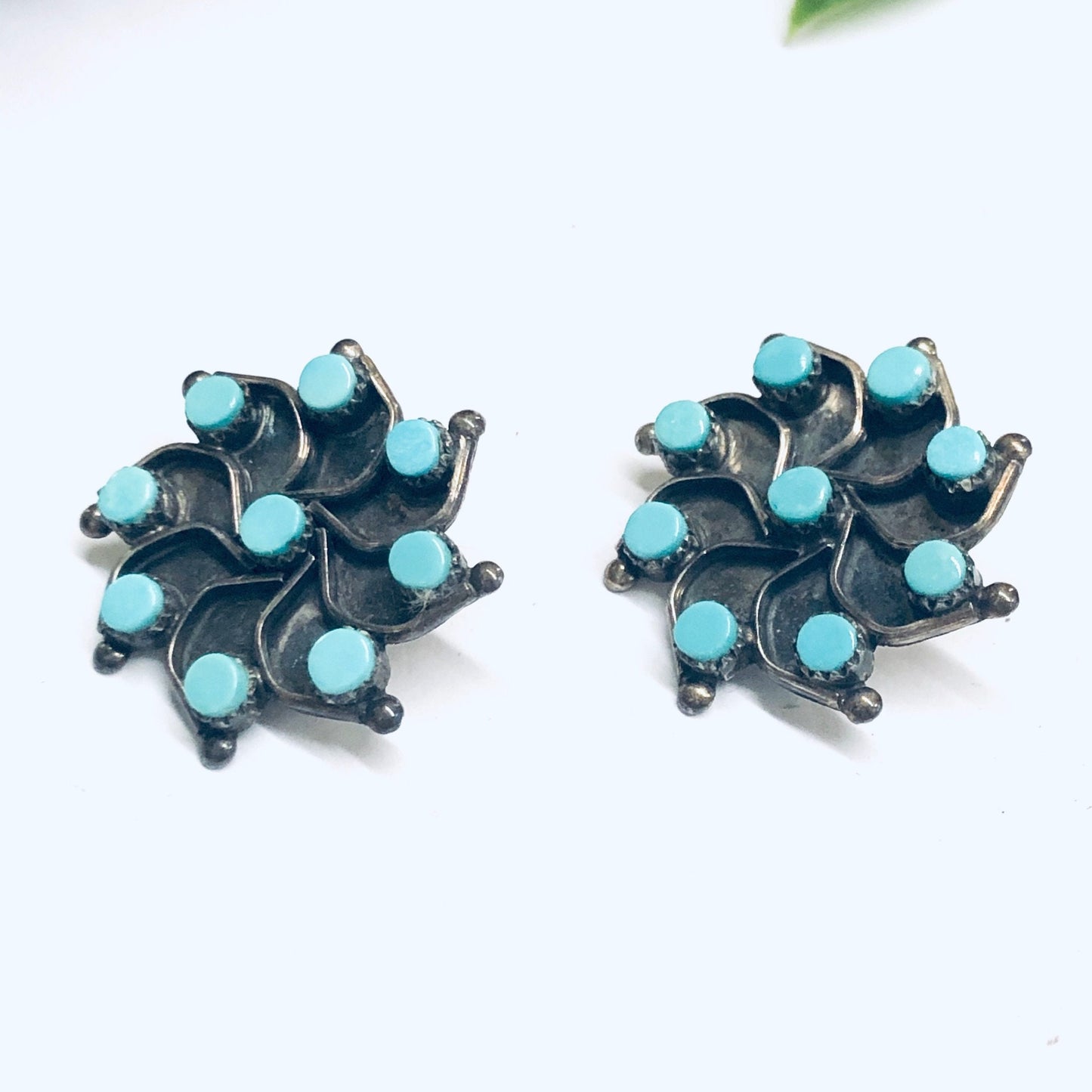 Vintage silver and turquoise star-shaped clip-on earrings on white background with green leaf