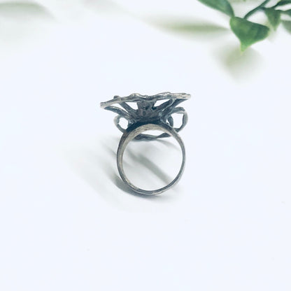 Silver spider ring with large, intricate spider design on minimalist background with green leaves, vintage silver insect jewelry statement ring, spooky spider ring