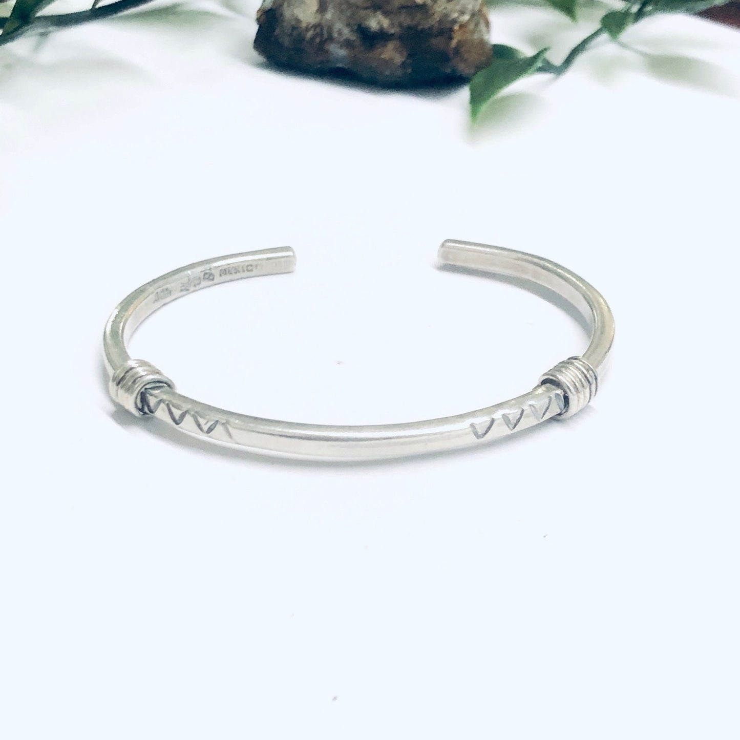 Vintage silver thin cuff bracelet on white background with leaves and rocks