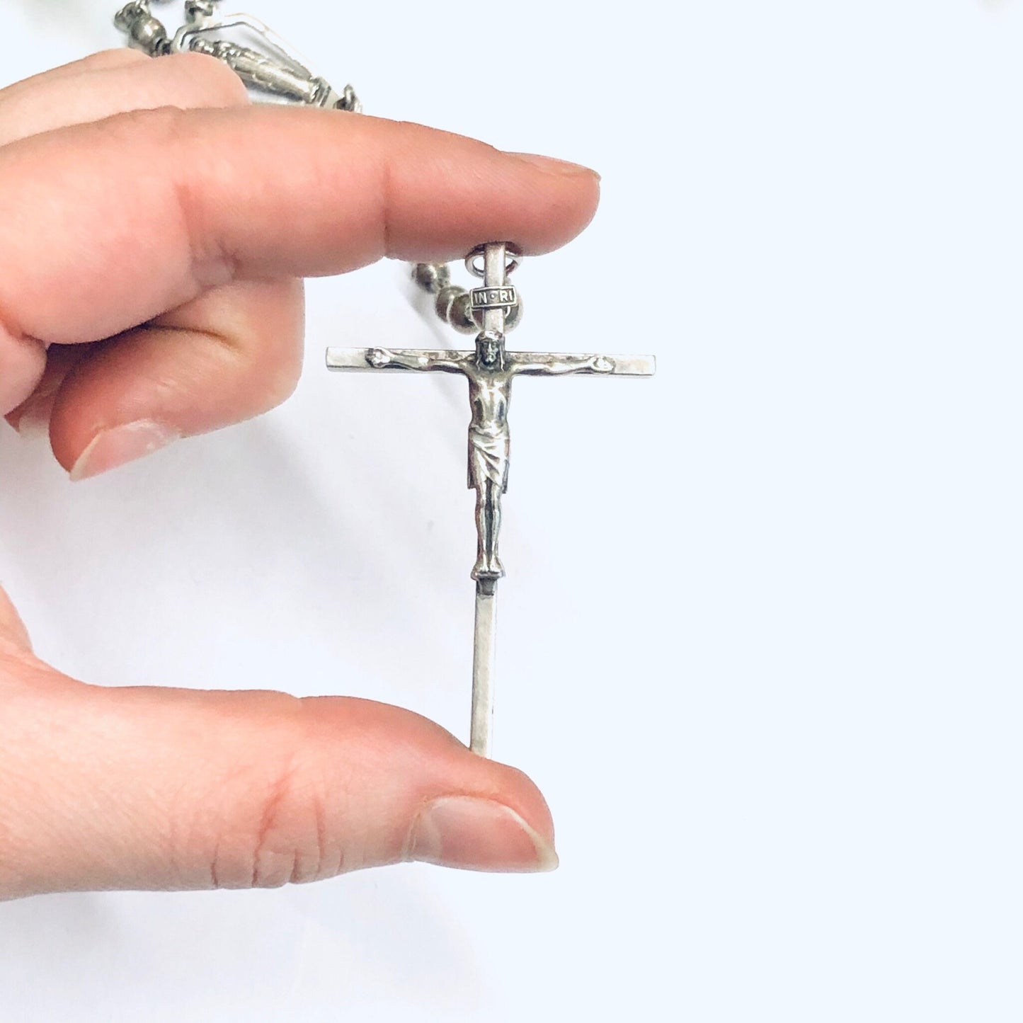 Silver rosary with crucifix held between fingers, religious prayer beads on white background