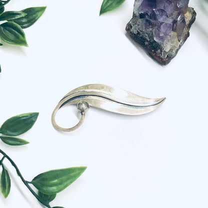 Silver modernist Taxco brooch in the shape of a lily of the valley leaf next to a purple amethyst crystal geode on a white background with green leaf accents