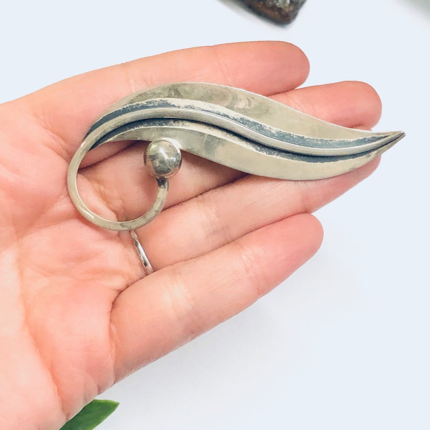 Vintage Taxco silver leaf brooch or pin held in a person's hand, made by Delfino, with a modernist wave design resembling a lily of the valley leaf from the midcentury modern period.