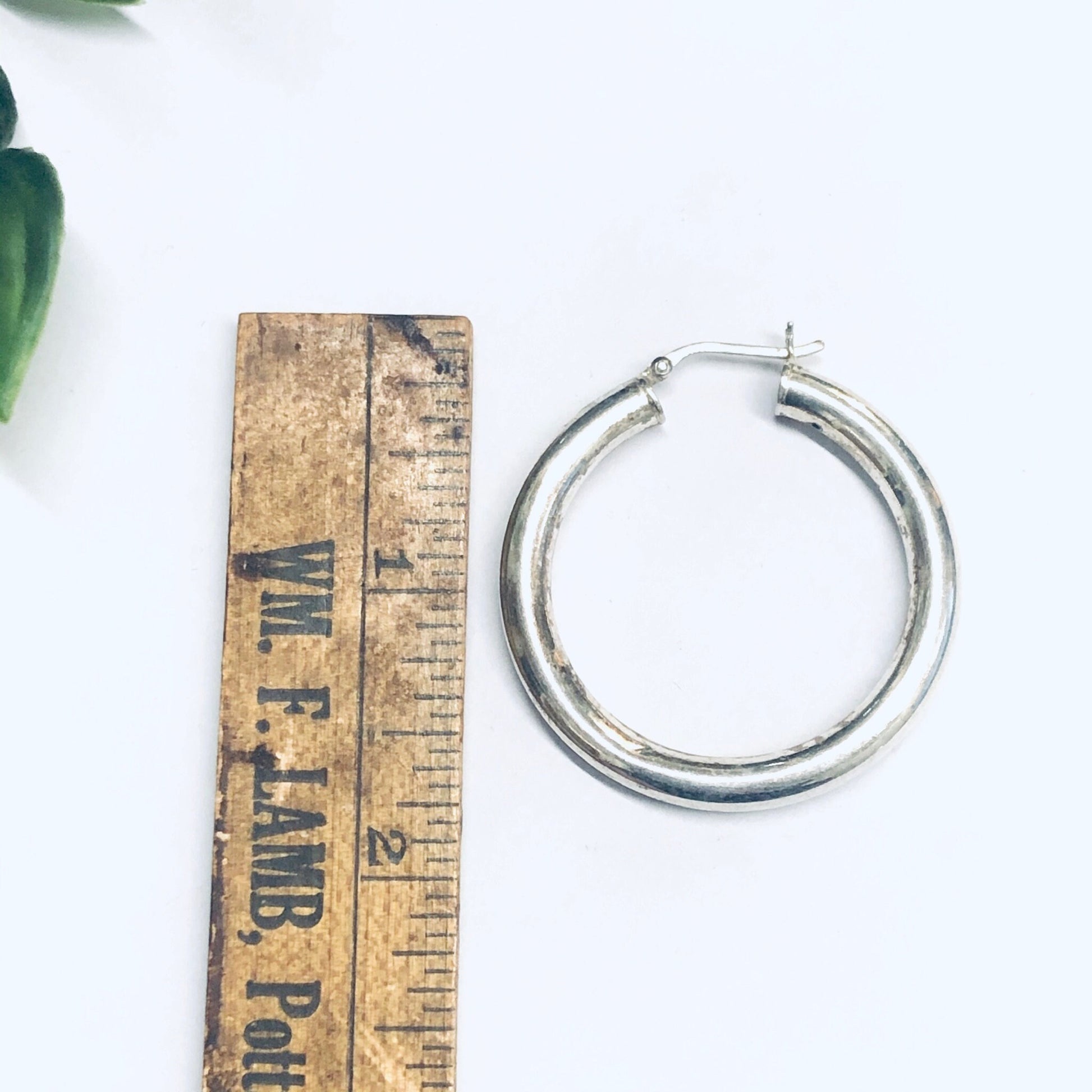 Silver hoop earrings placed next to vintage wooden ruler for size comparison, medium sized hollow silver hoops for pierced ears