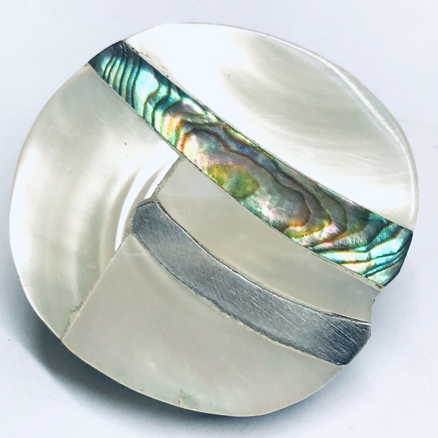 Vintage abalone shell clip-on earrings with abstract curved mother-of-pearl inlays, displayed on a white ceramic plate