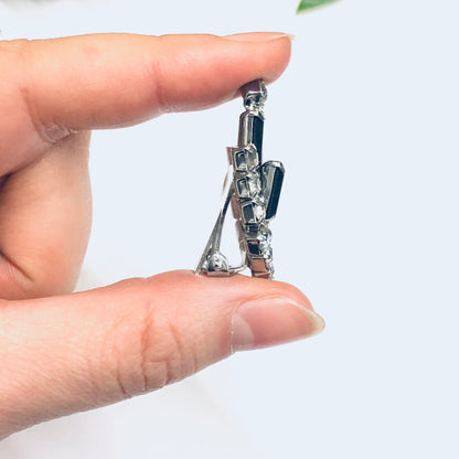 Black and silver rhinestone clip-on earrings held between fingers against a white background