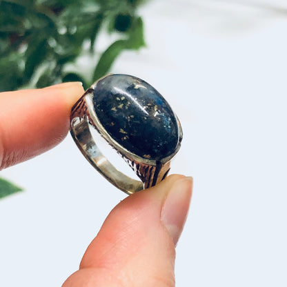 Vintage silver ring with large oval blue lapis lazuli gemstone held up in front of green foliage background