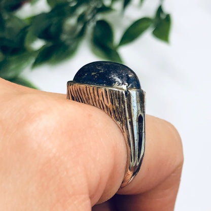 Vintage silver ring with deep blue lapis lazuli stone on finger, surrounded by green leaves. Unique cocktail ring, statement jewelry piece, perfect for a bold fashion look or special occasion gift.