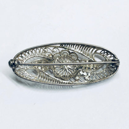 Vintage silver brooch with intricate floral design featuring cut-out details, creating a delicate and ornate piece of antique jewelry suitable as a decorative pin.