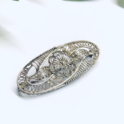 Vintage silver brooch featuring an ornate cut out flower design, delicate silver pin with intricate detailing, piece of ornate vintage jewelry.