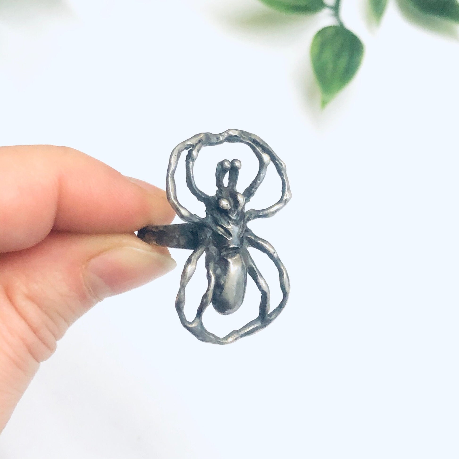 Silver spider ring held in front of green leaves, vintage large statement insect jewelry ring, spooky spider design silver ring