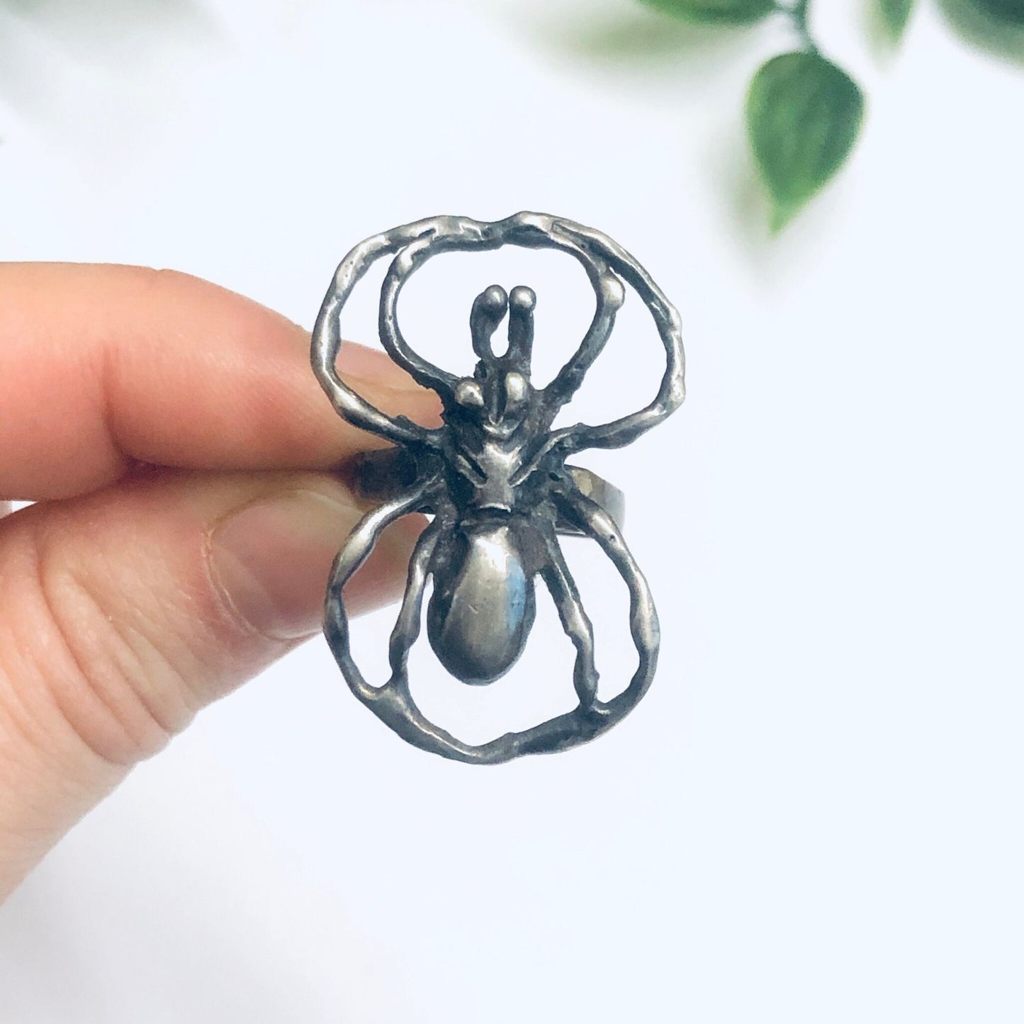 Silver spider ring held in front of green leaves, vintage large statement insect jewelry ring, spooky spider design crafted in oxidized silver metal.