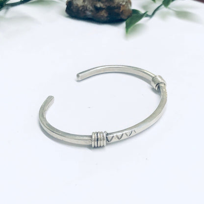 Vintage silver thin cuff bracelet on white background near rocks and leaves, simple small minimalist metal bangle bracelet jewelry