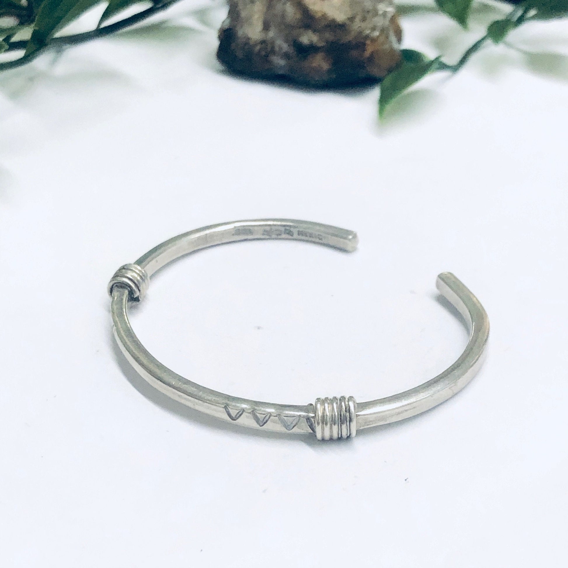 Vintage silver thin cuff bracelet with simple design resting on white surface near greenery