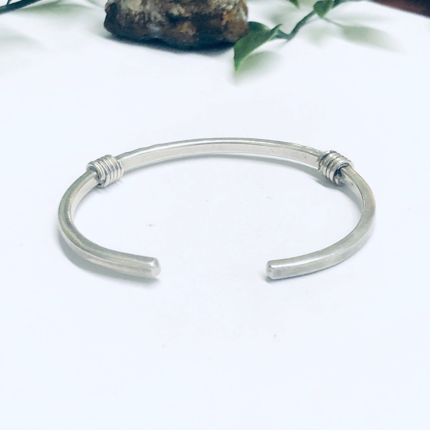 Vintage silver thin cuff bracelet placed on white background next to rocks and greenery