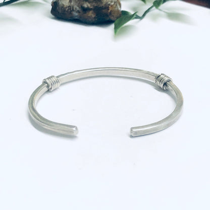 Vintage silver thin cuff bracelet placed on white background next to rocks and greenery