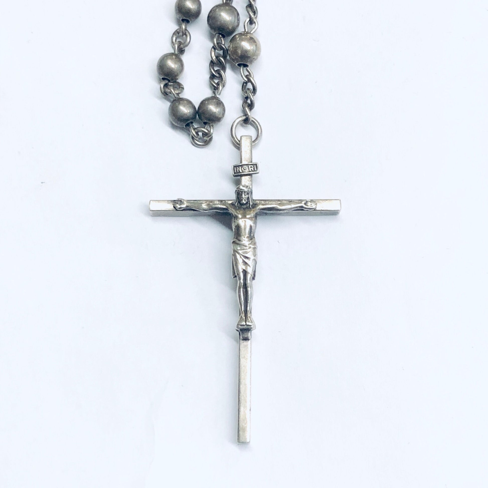 Silver rosary prayer beads with crucifix pendant on a white background, religious jewelry closeup