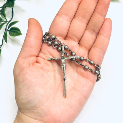 Silver rosary beads with crucifix held in open palm against white background with green leaves