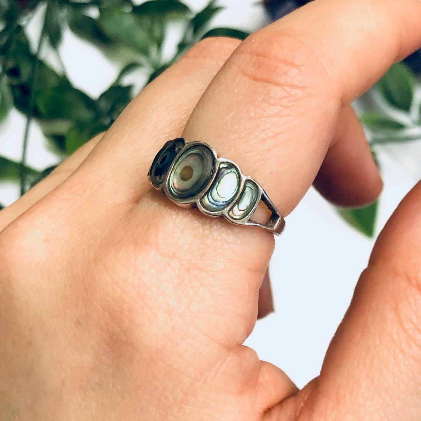 Vintage abalone and silver statement ring displayed on a person's hand in front of green foliage background