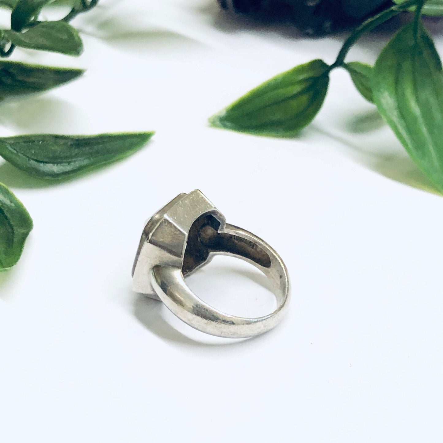 Large silver statement cocktail ring with unique geometric design, seen on white background with green leaves, perfect as a promise ring or eye-catching jewelry piece from a vintage collection.