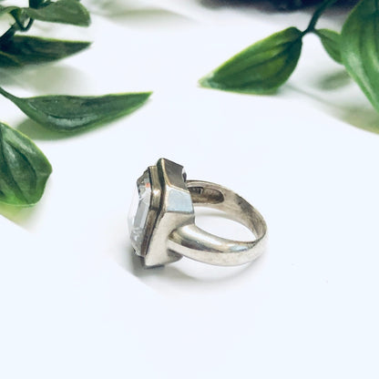 Large silver cocktail statement ring with unique overlapping band design, set against green leaves on a white background, perfect as a promise ring or eye-catching vintage jewelry piece.