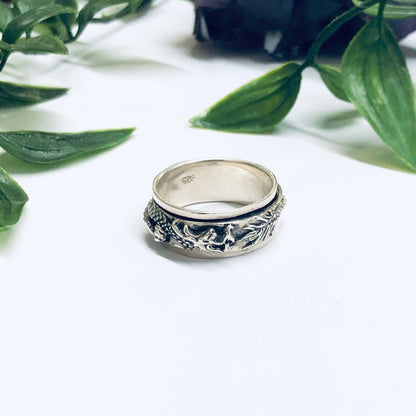 Vintage silver dragon spinner meditation ring on white surface with green leaves in background