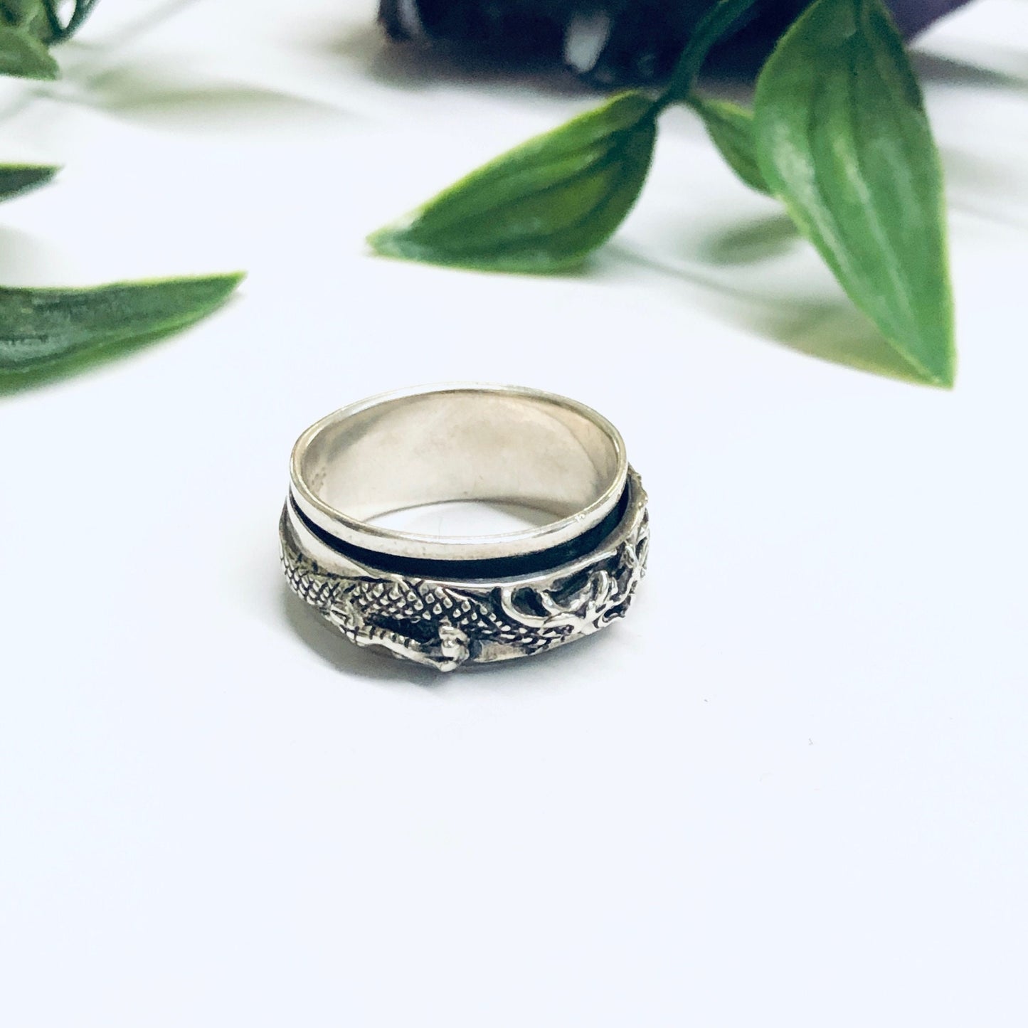 Vintage silver dragon spinner ring on white surface with green leaves in background