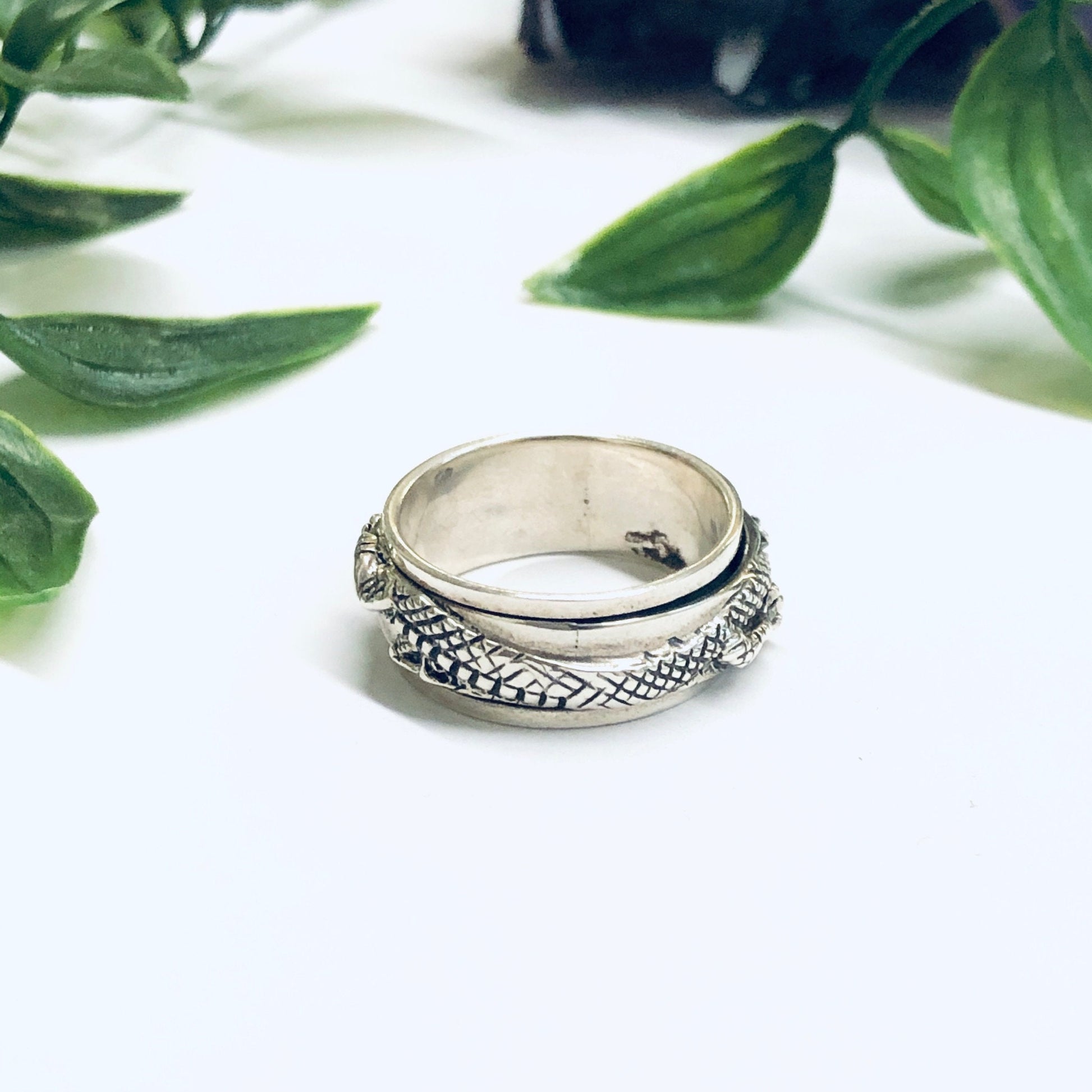 Vintage silver dragon spinner meditation ring with thin band, surrounded by green leaves on white background.