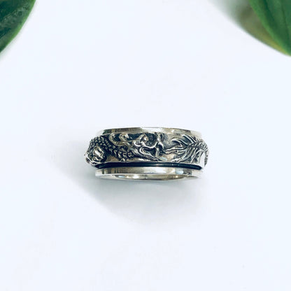 Vintage silver dragon spinner meditation ring with thin band on white background surrounded by green leaves