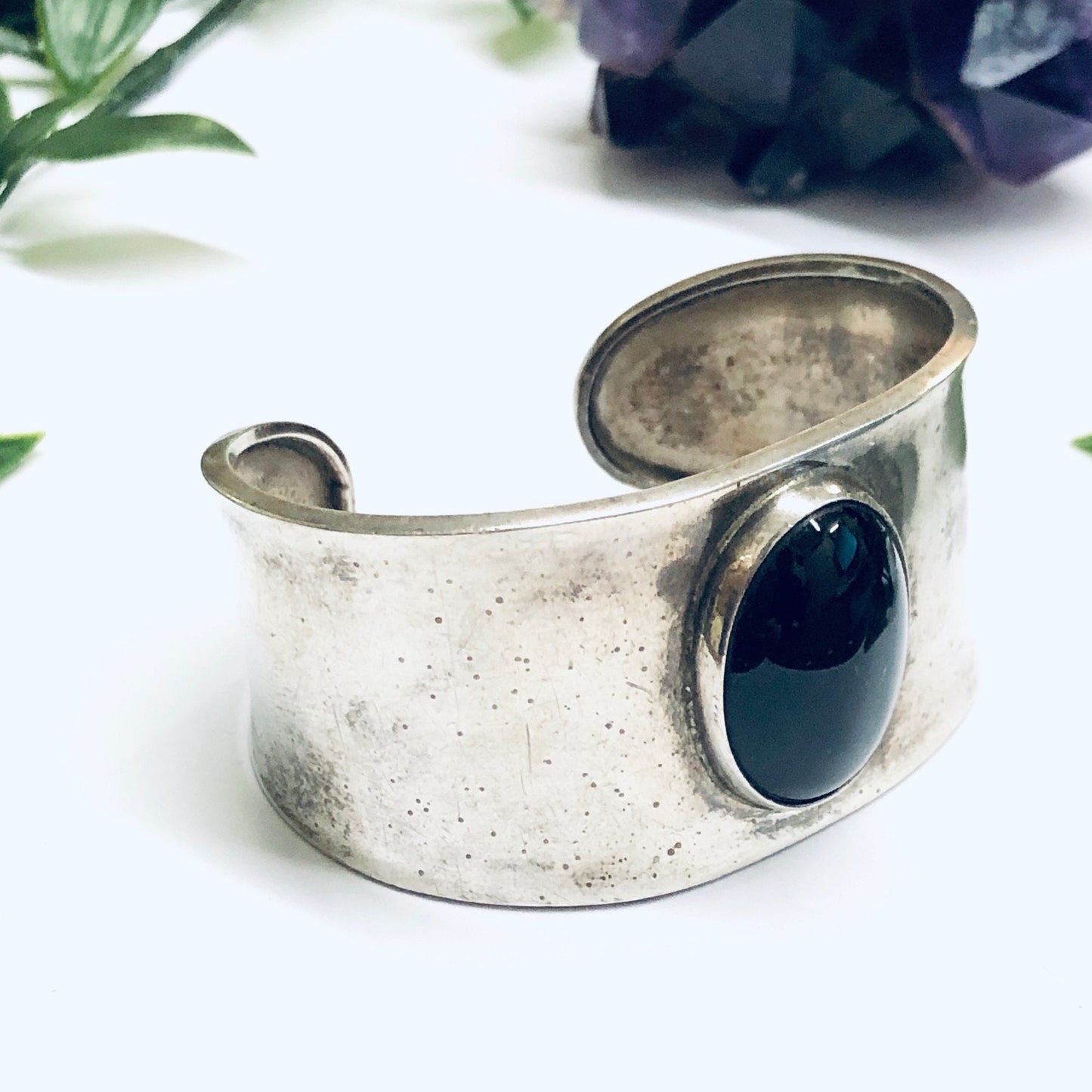 Vintage silver cuff bracelet featuring a large oval onyx stone, crafted in a wide, textured silver band design. The deep black onyx provides a striking contrast against the aged patina of the silver, creating a bold and timeless piece of jewelry.