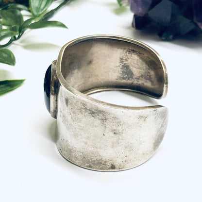 Vintage silver cuff bracelet with onyx stone on a white background with greenery