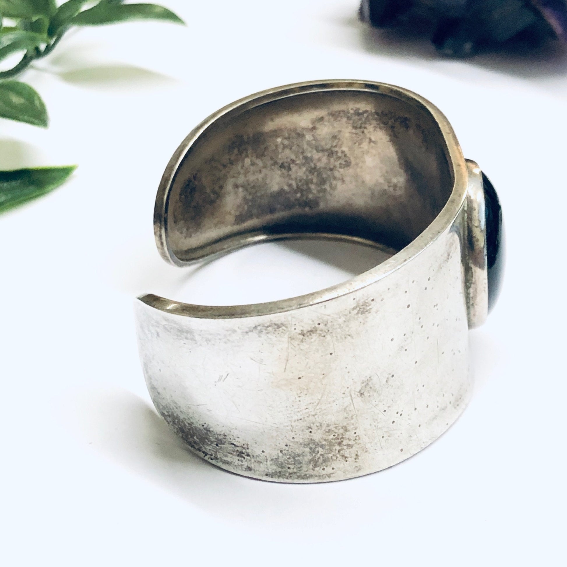 Vintage silver cuff bracelet with black onyx stone on white background with greenery