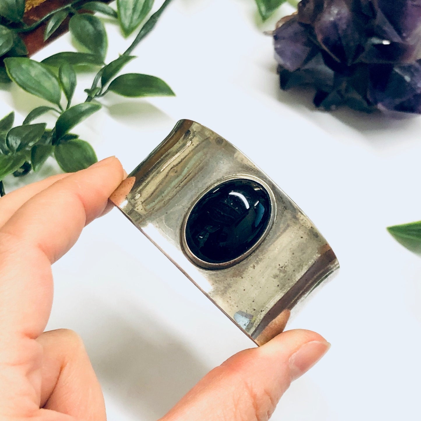 Vintage silver cuff bracelet with oval black onyx stone set in the center, held in hands with greenery in the background.