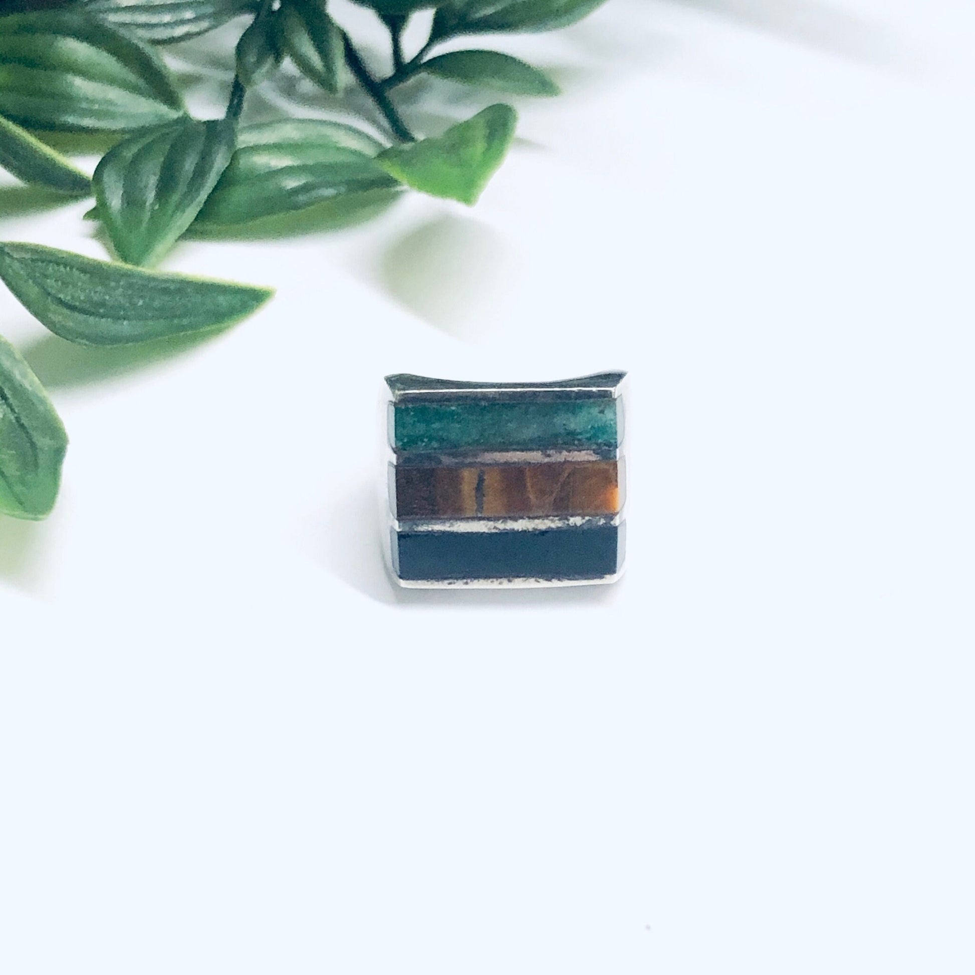 Vintage silver ring with natural black onyx and tiger's eye inlaid stones, handcrafted men's jewelry, displayed on white background with green leaves.