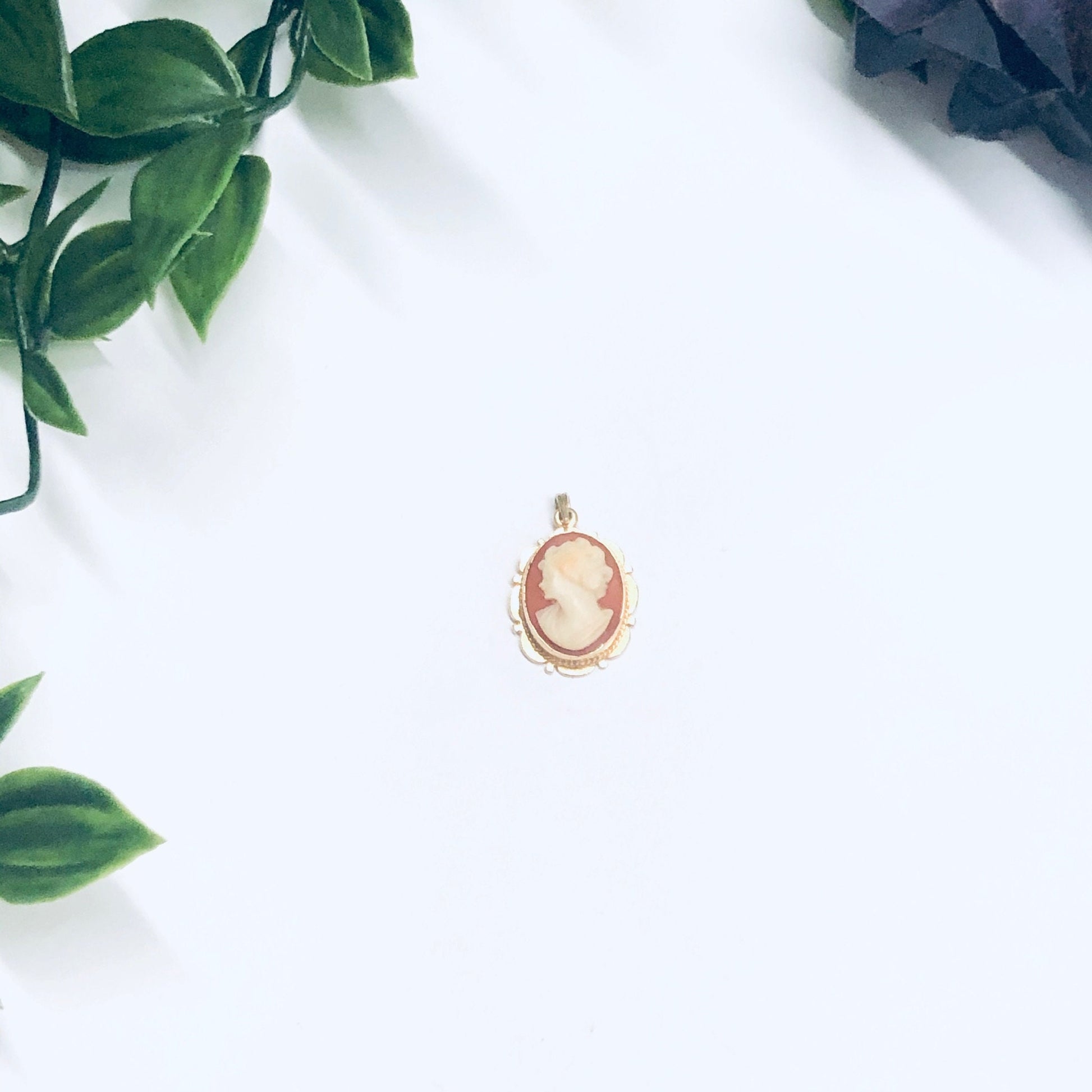 14K yellow gold vintage cameo pendant surrounded by leaves on a white background