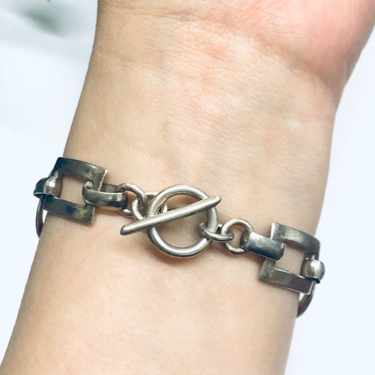 Silver geometric link bracelet with toggle closure on person's wrist