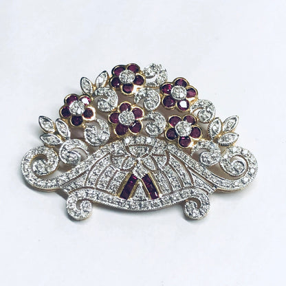 Vintage 18K yellow gold brooch pin featuring rubies and diamonds in an intricate floral design, with curving lines and detailed diamond accents creating an elegant ruby flower jewelry piece.