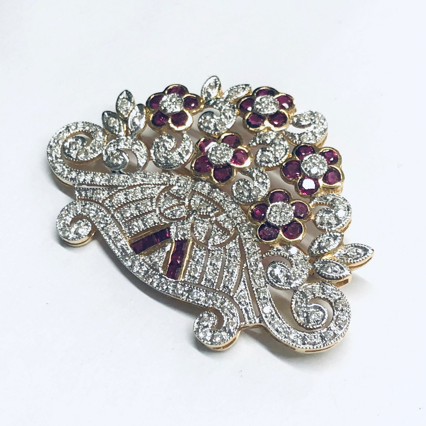 Vintage 18K yellow gold brooch pin with ruby and diamond floral design, featuring swirling lines of round brilliant cut diamonds accented by ruby flower petals in a gorgeous statement piece of ruby jewelry.