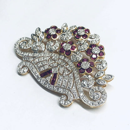 Vintage 18K yellow gold brooch pin with ruby and diamond floral design, featuring swirling lines of round brilliant cut diamonds accented by ruby flower petals in a gorgeous statement piece of ruby jewelry.