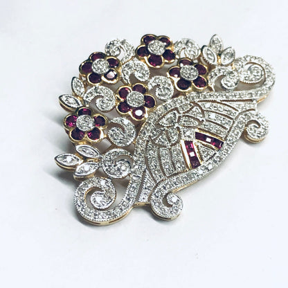 Vintage 18K yellow gold brooch pin with rubies, diamonds and intricate floral design. Stunning ruby and diamond encrusted brooch crafted in luxurious 18K gold, featuring swirling leaves and flower petals adorned with glittering precious gemstones.