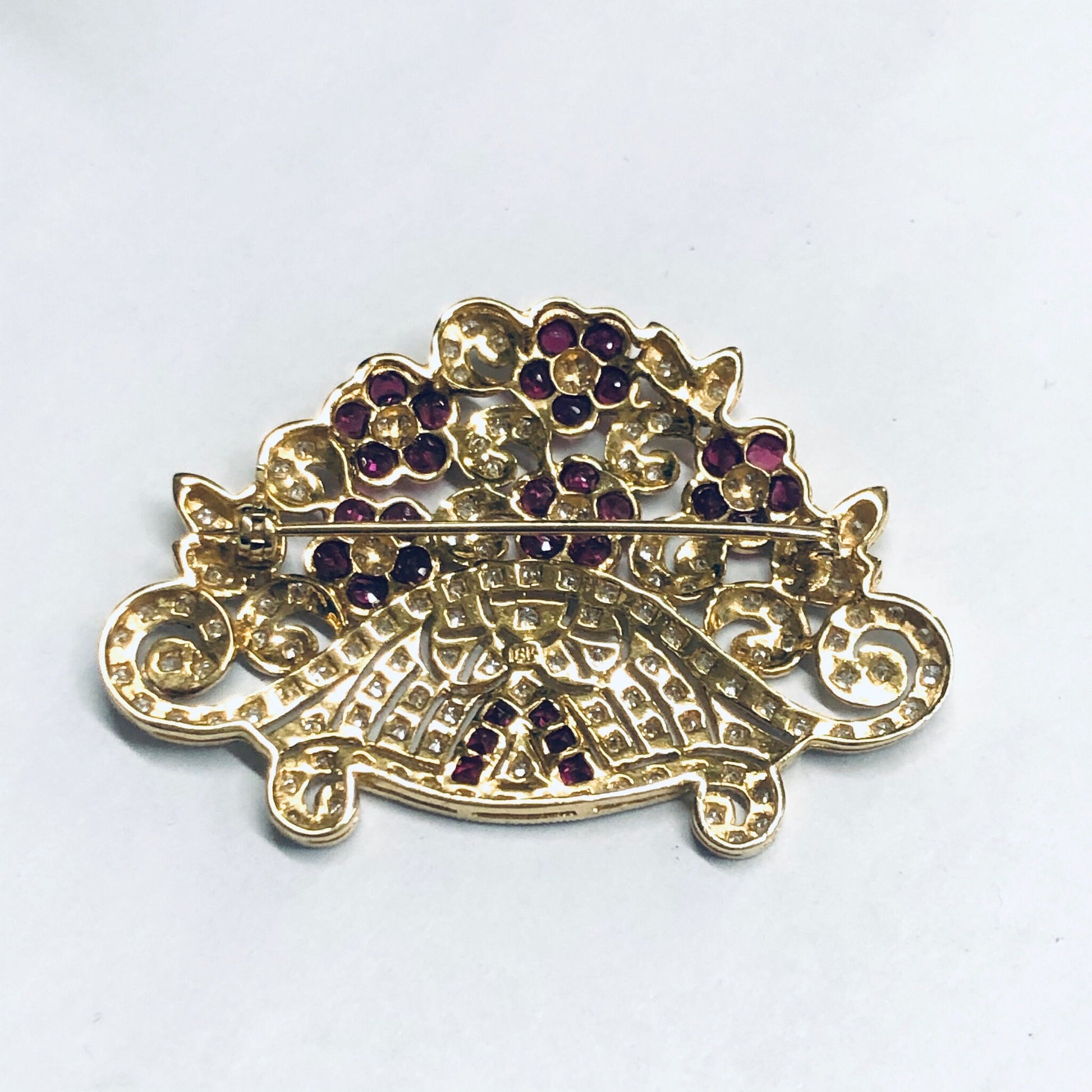 Vintage 18K yellow gold brooch pin with ruby and diamond flower design, featuring intricate metalwork and gemstone accents in a decorative floral motif.