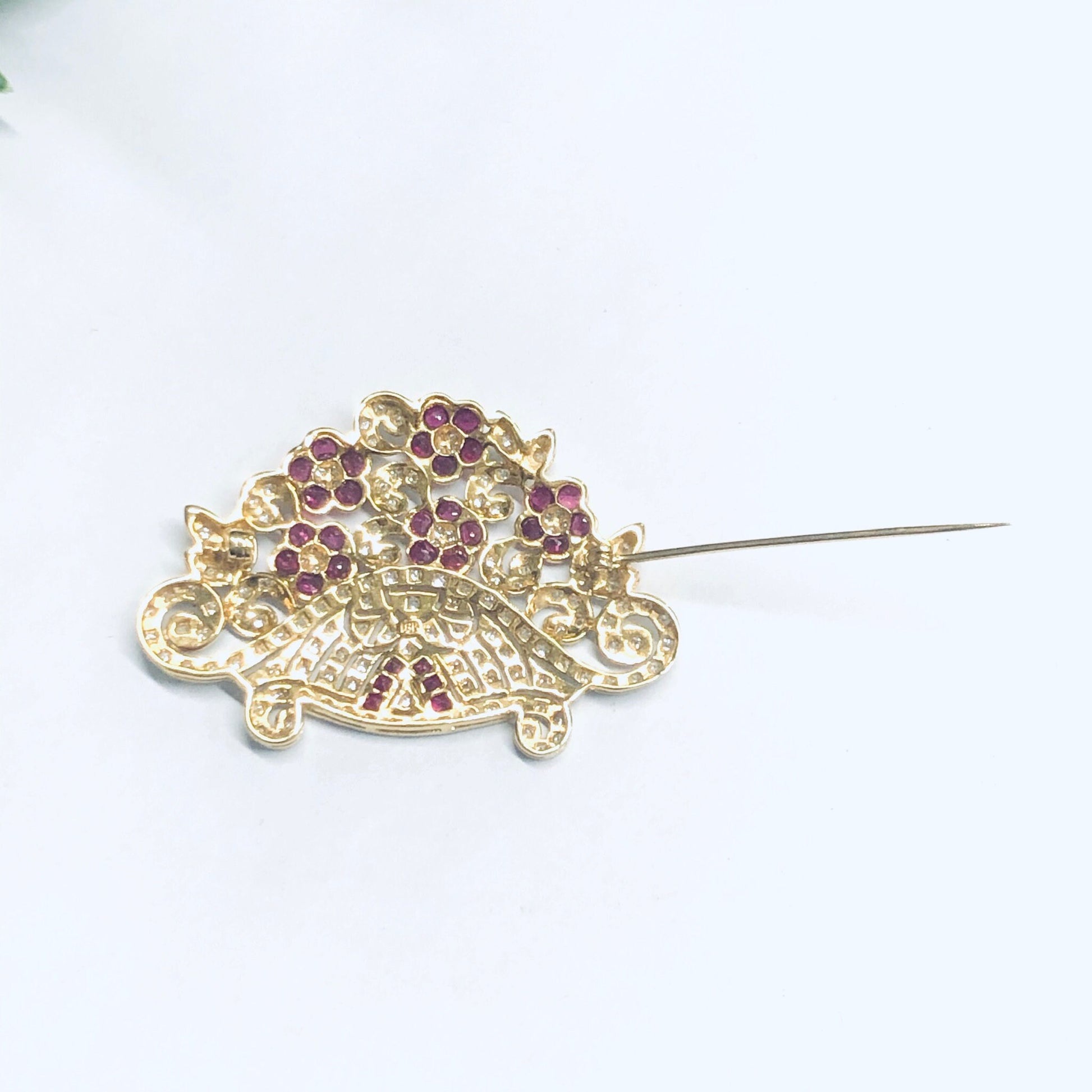 Vintage 18K yellow gold brooch pin with ruby and diamond flower design against a white background.