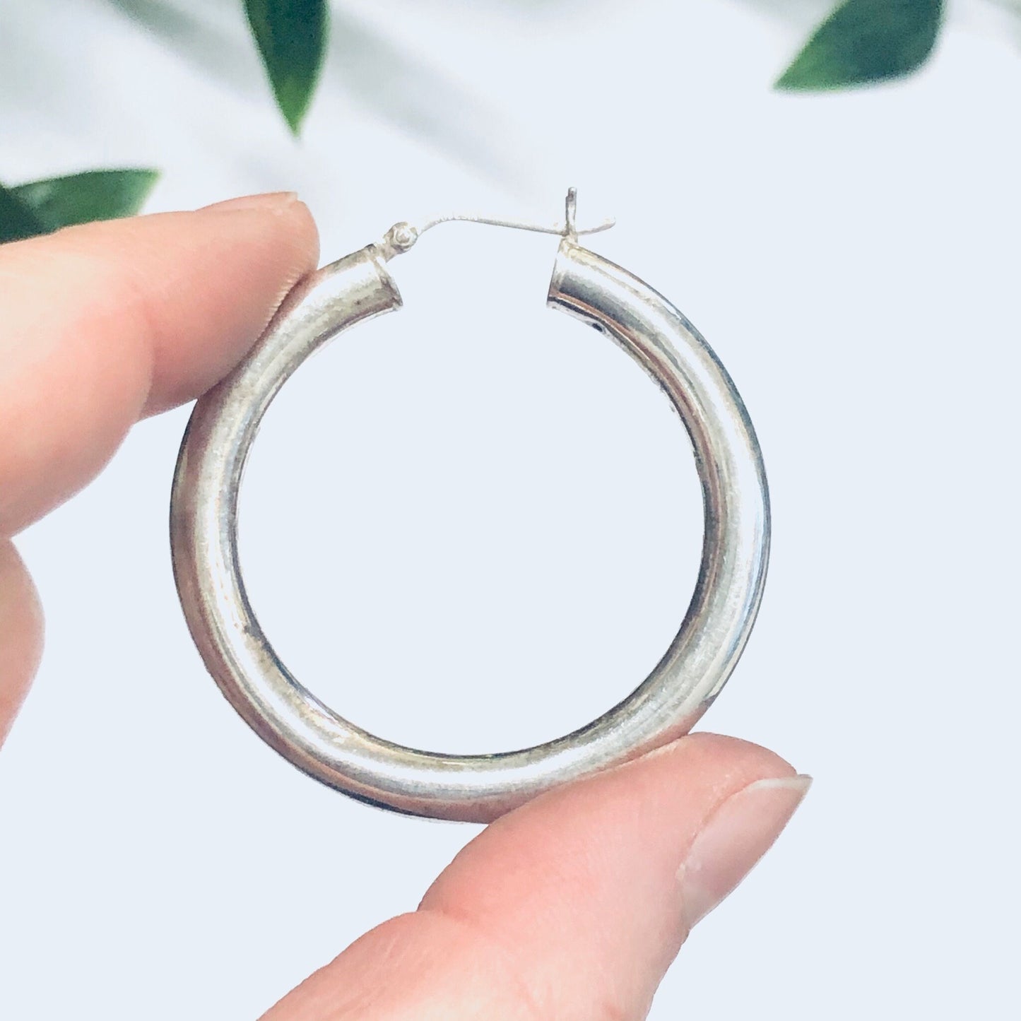 Silver hoop earrings held in hand with green leaves in soft focus background