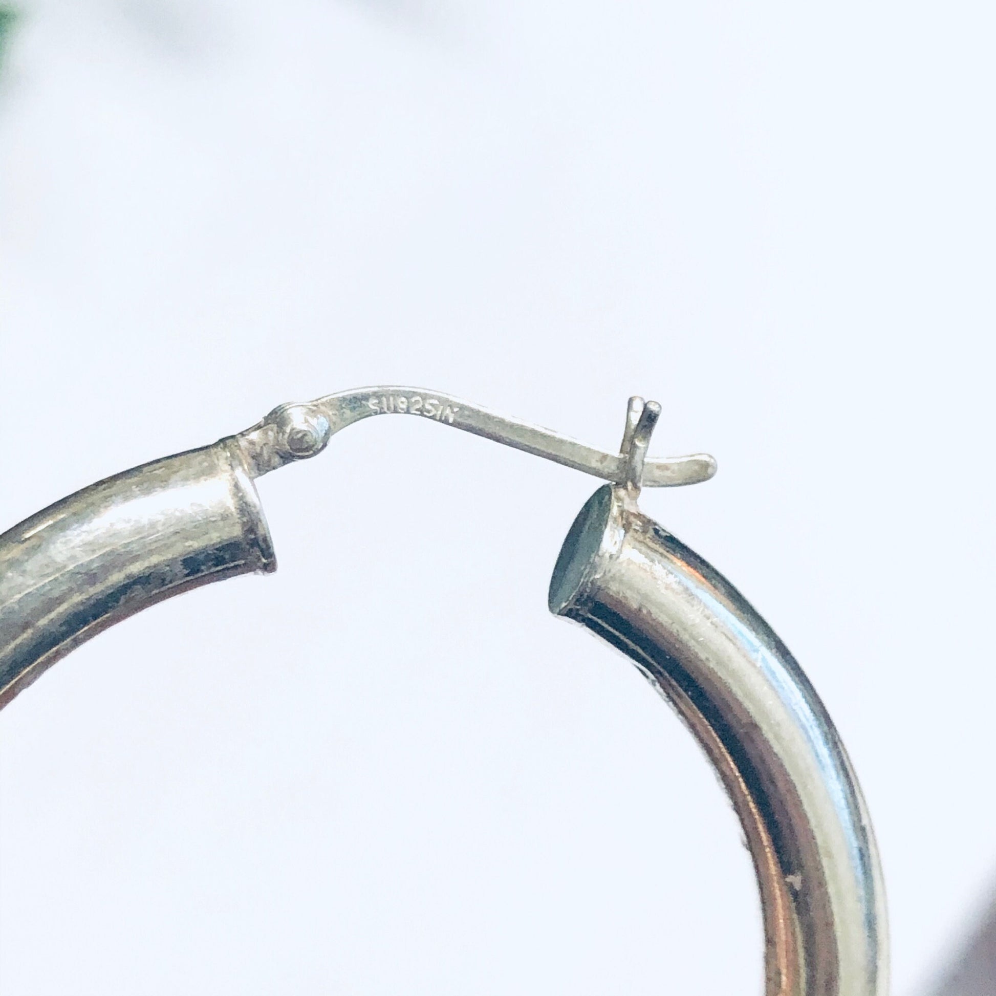 Silver hoop earrings on a white background, showing the connecting point where the hollow hoop attaches to the post that goes through the pierced ear.