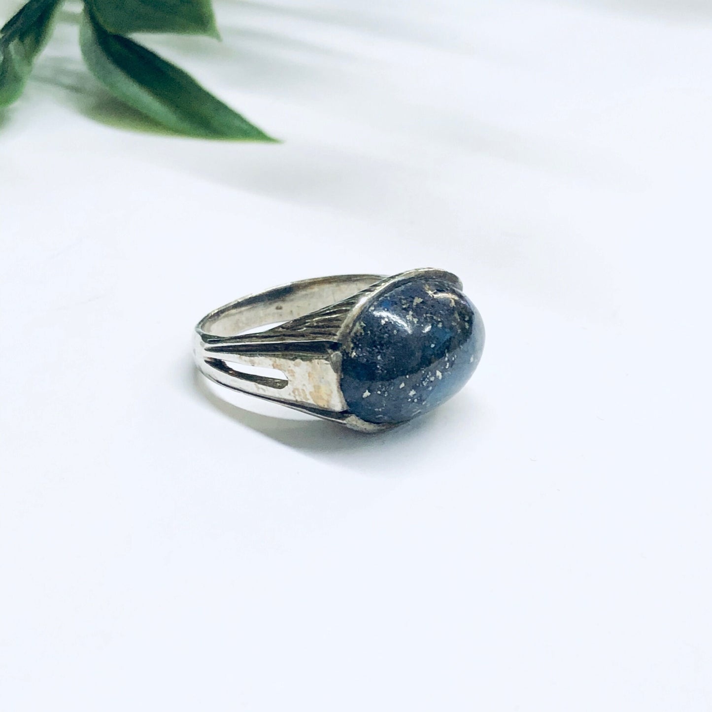 Vintage silver ring with oval blue lapis lazuli cabochon stone on white background with green leaves