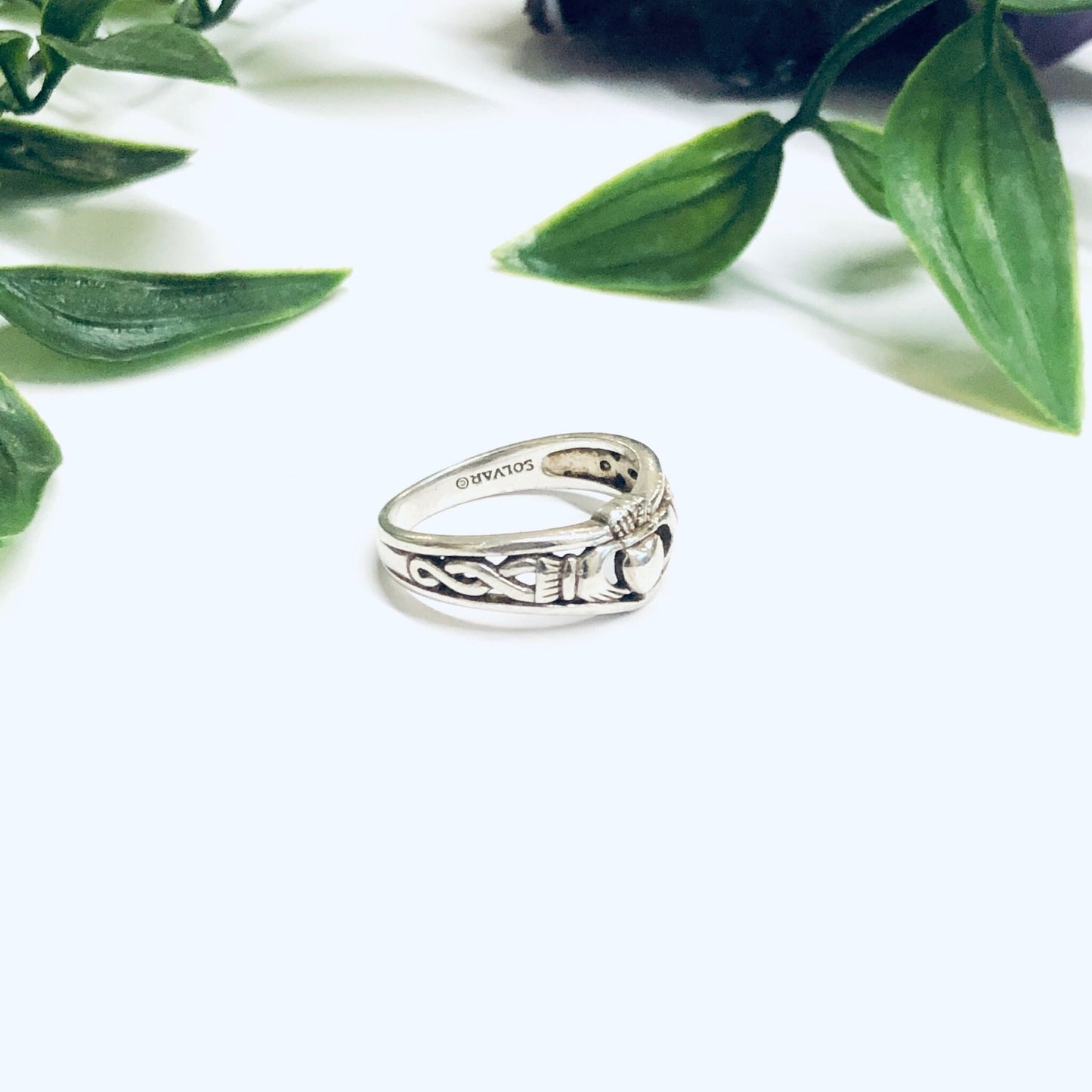 Silver Claddagh ring with heart in hands design amongst green foliage