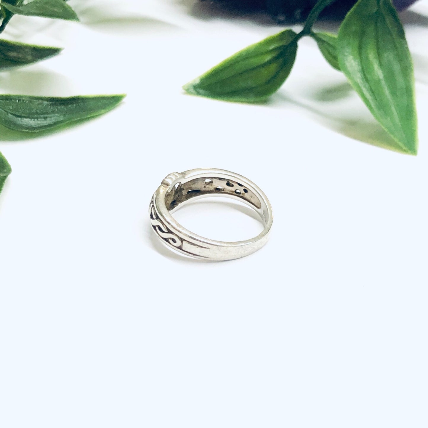 Irish Claddagh silver ring on white surface with green leaves