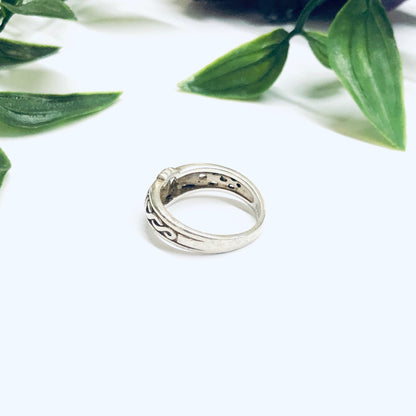 Irish Claddagh silver ring on white surface with green leaves