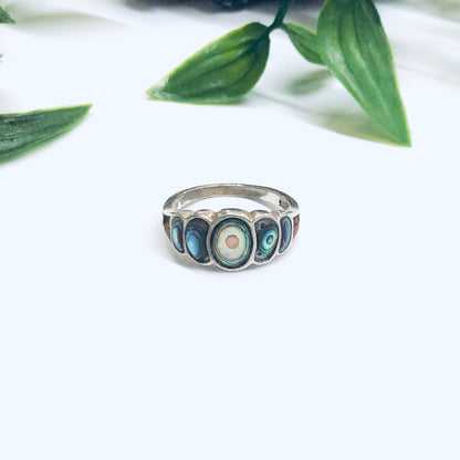 Vintage abalone and silver statement ring displayed on white surface with green leaves in soft focus background