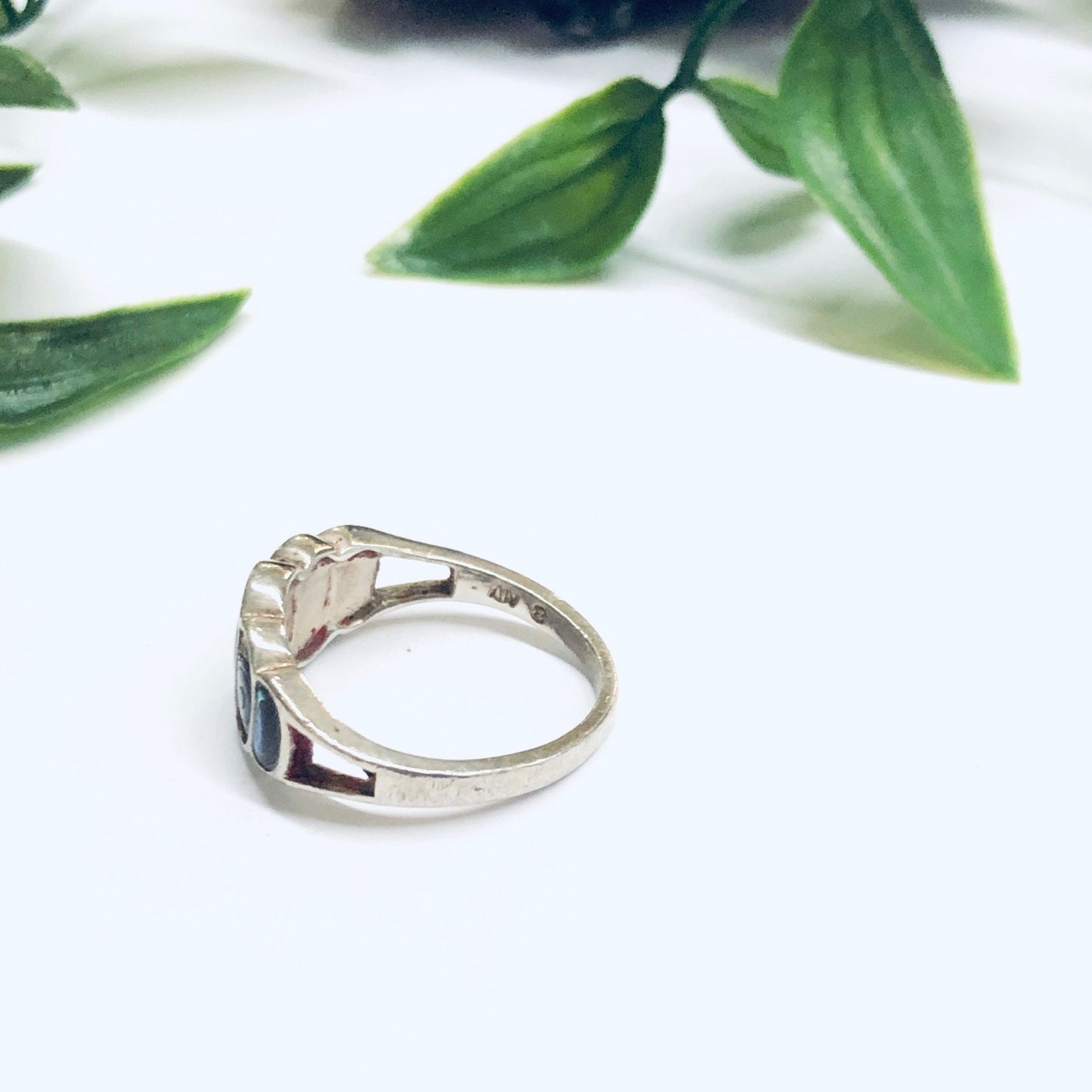 Vintage silver abalone shell ring displayed on white surface with green leaves in soft focus background