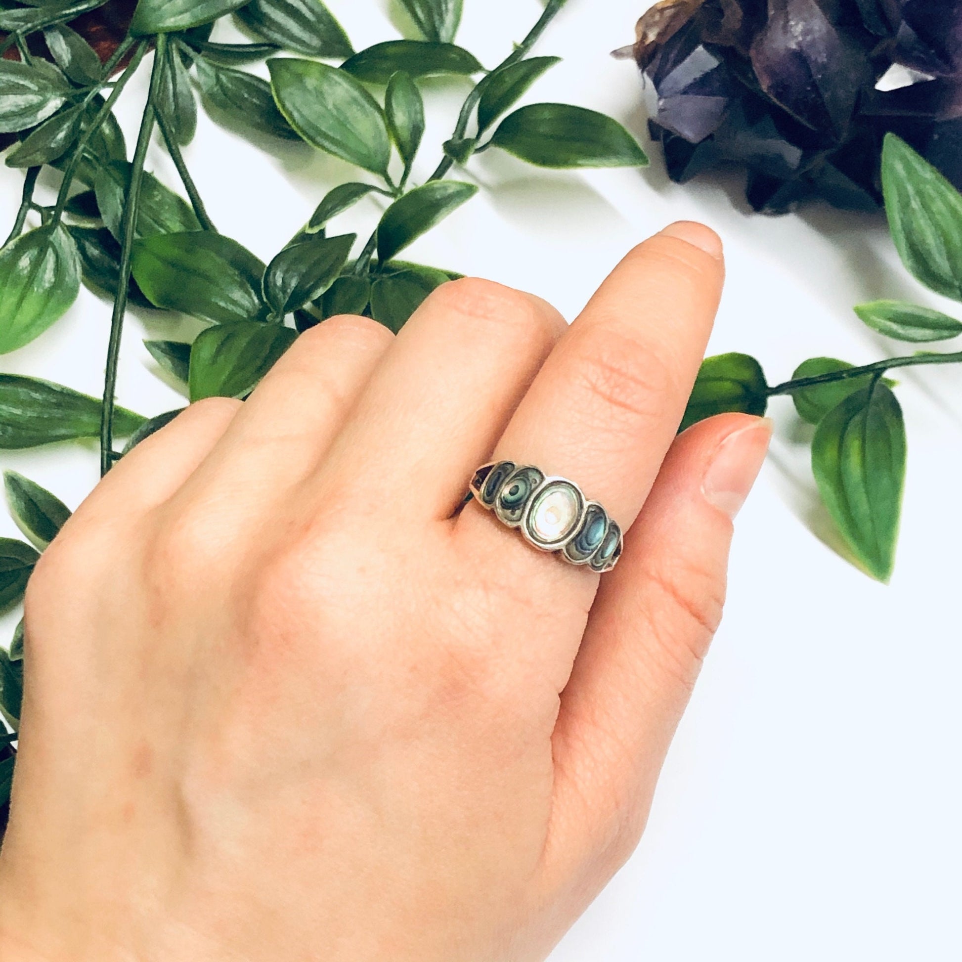 Vintage abalone and silver statement ring showcased on a hand with greenery in the background.